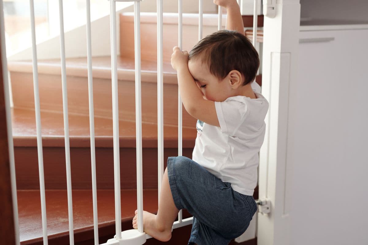 A toddler climbing a white safety gate installed at the top of a staircase