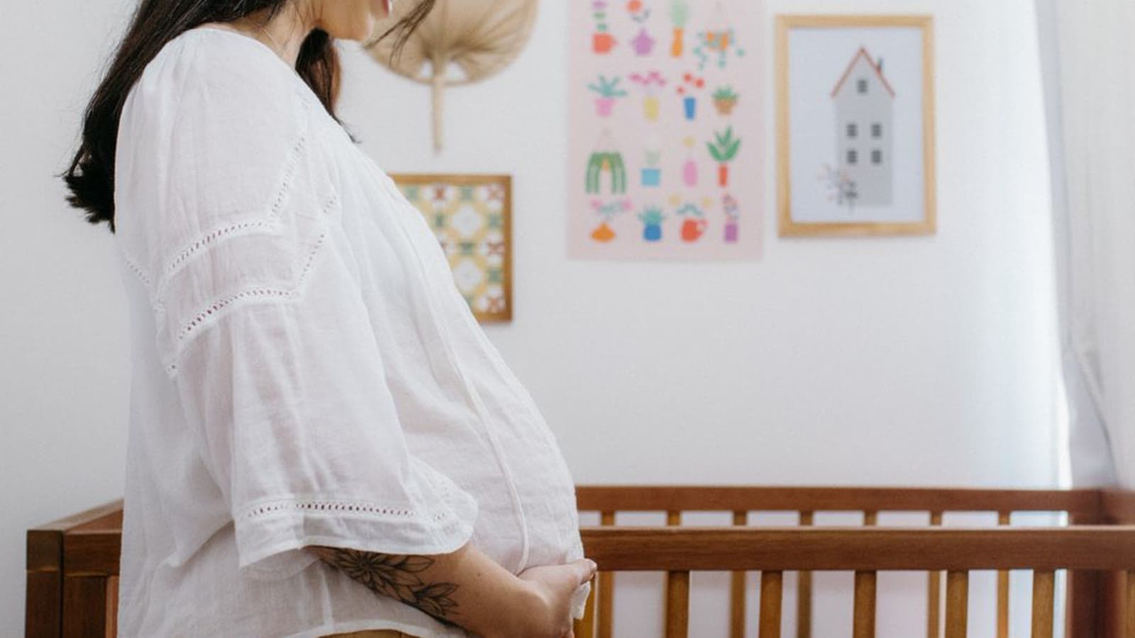 A pregnant woman standing beside a wooden crib in a nursery