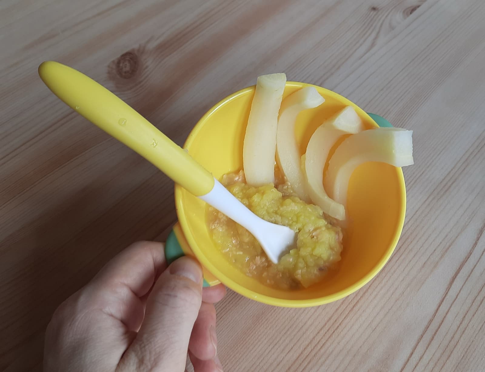 Homemade baby food puree and soft steamed fruit slices in a yellow baby bowl with a soft-tip spoon