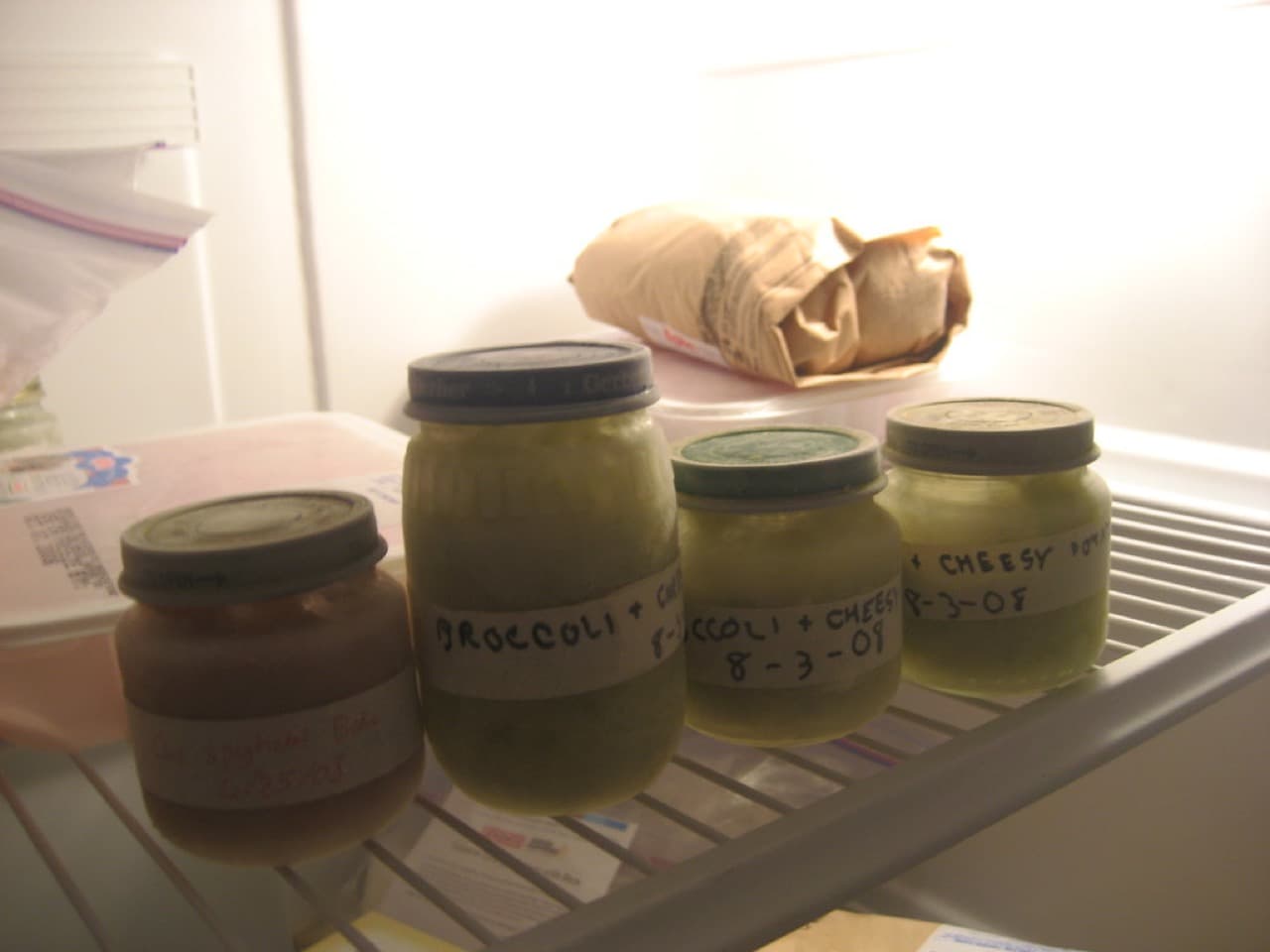 Labeled glass jars of homemade baby food puree lined up on a refrigerator shelf