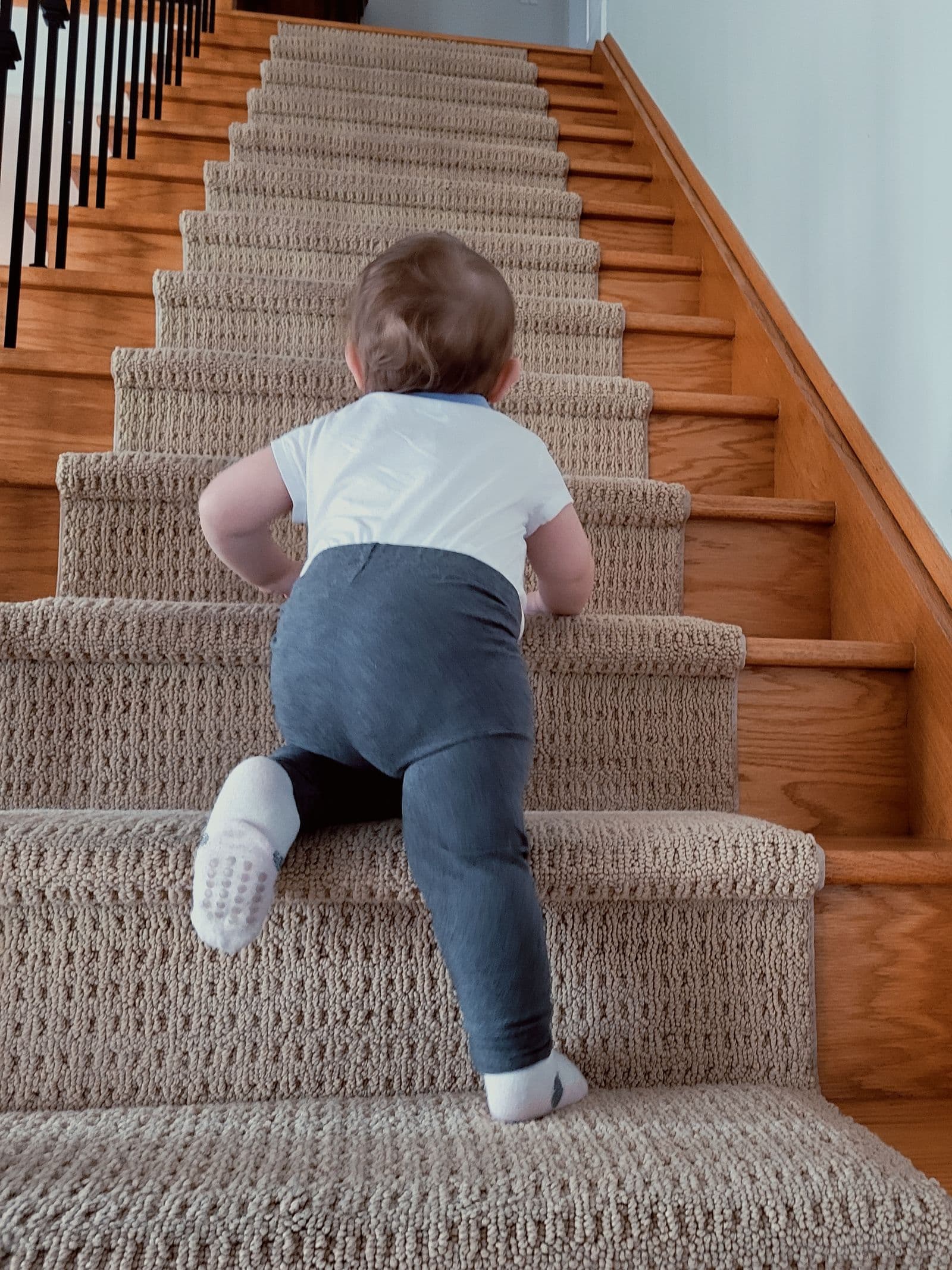 A baby climbing a staircase at home, where a safety gate is needed