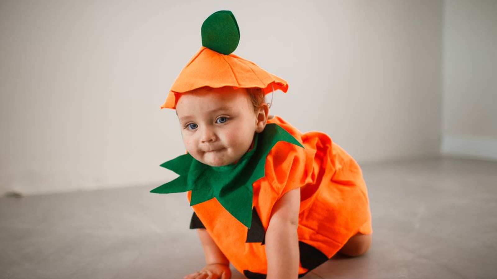 A baby in an orange pumpkin costume crawling on the floor