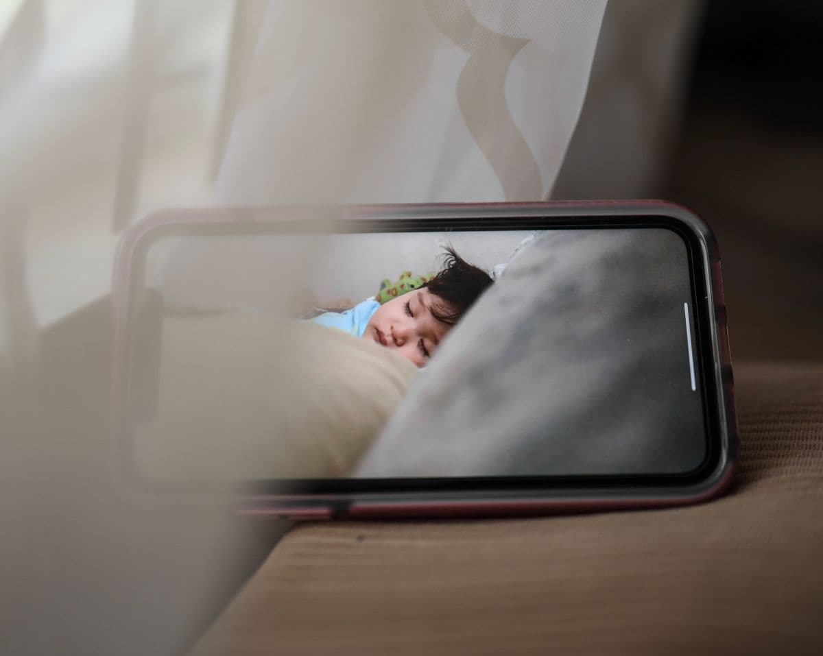 A smartphone propped on a couch arm showing a live baby monitor video feed of a sleeping child