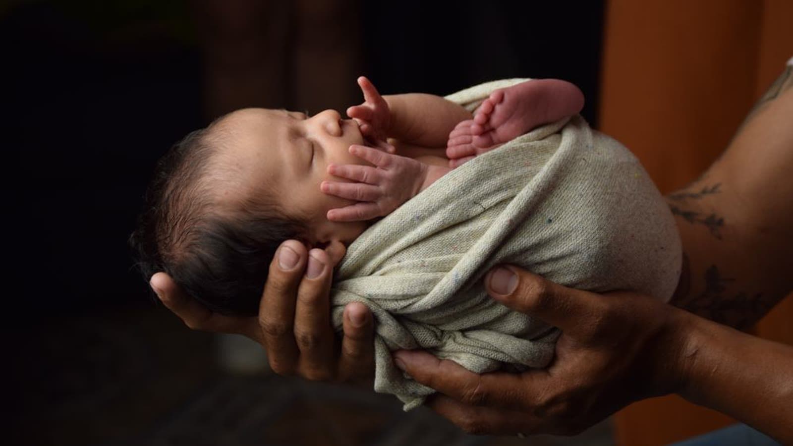 A newborn swaddled in a soft blanket and cradled in adult hands