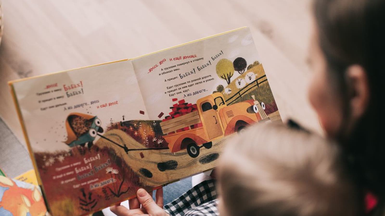 A mother reading an illustrated book with a toddler on her lap