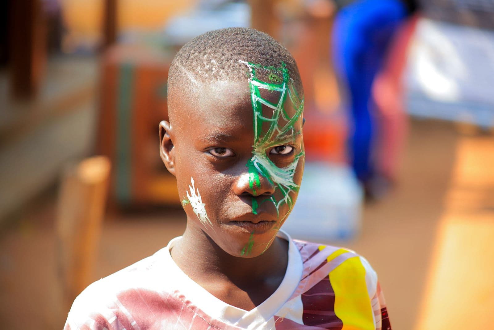A boy with a green and white spider-web design face-painted over one side of his face