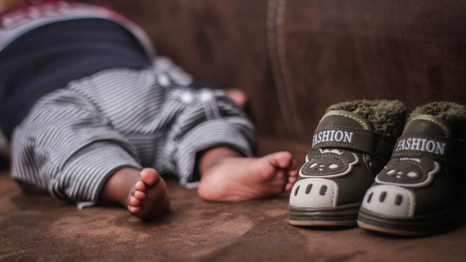 A baby's bare feet beside small animal-themed shoes on a couch