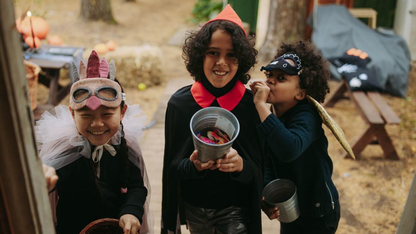 Three school-age children in Halloween costumes trick-or-treating with candy buckets