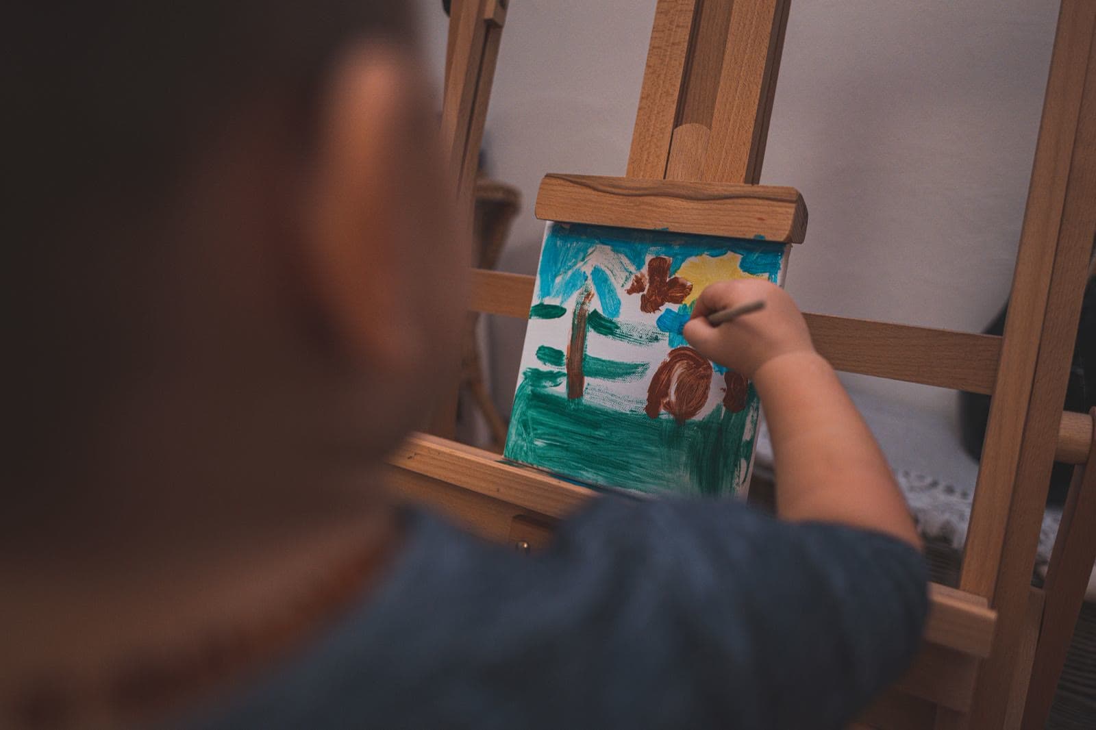 A young child painting on a canvas at a wooden easel