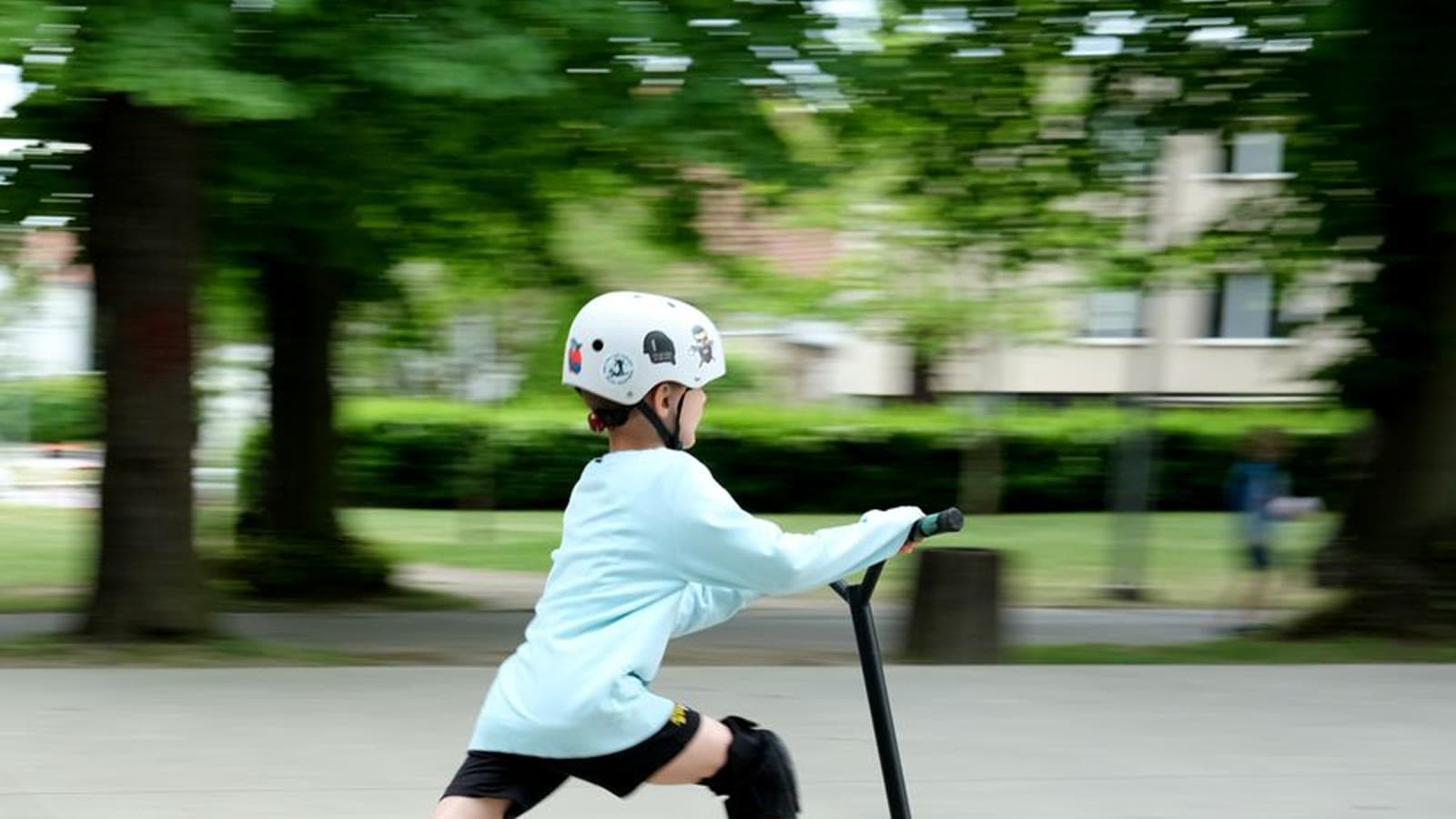 A boy riding a kick scooter on a path while wearing a blue helmet and knee pads