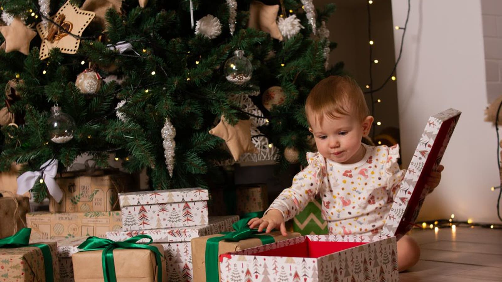 A toddler opening a Christmas present beside a decorated tree