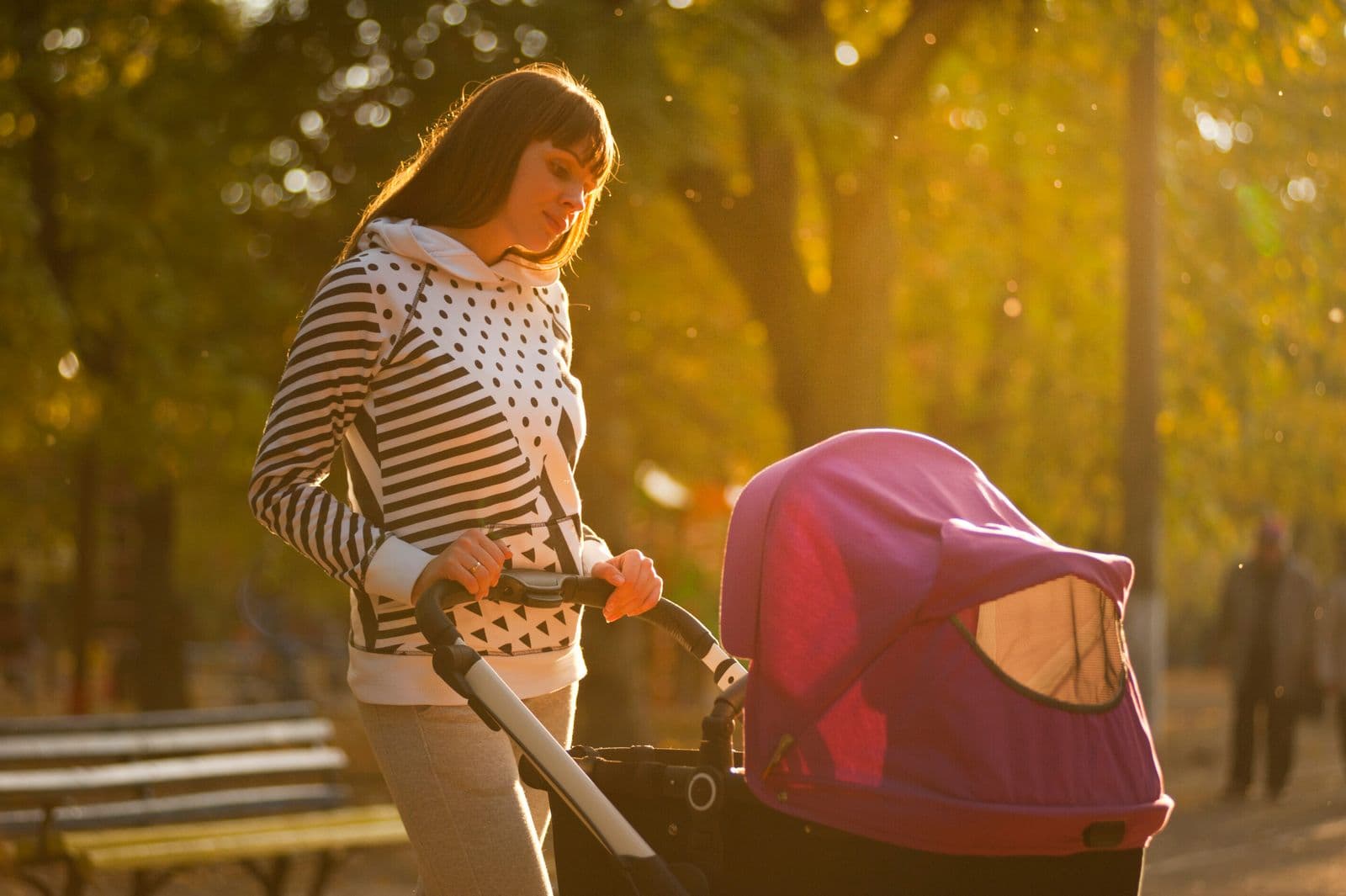 A parent pushing a stroller on a walk through a sunny park