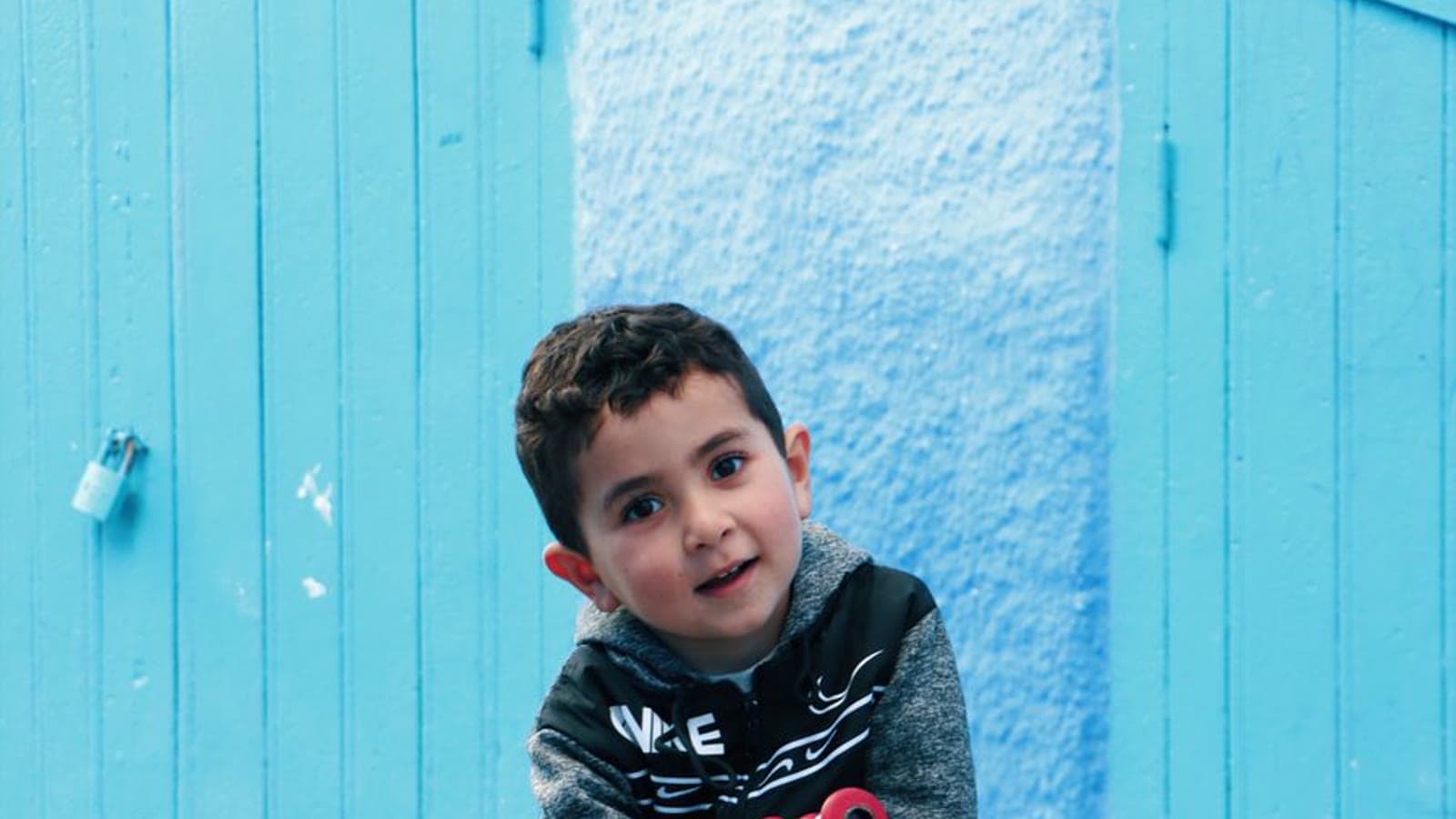 A young boy riding a small red balance bike on a cobblestone street