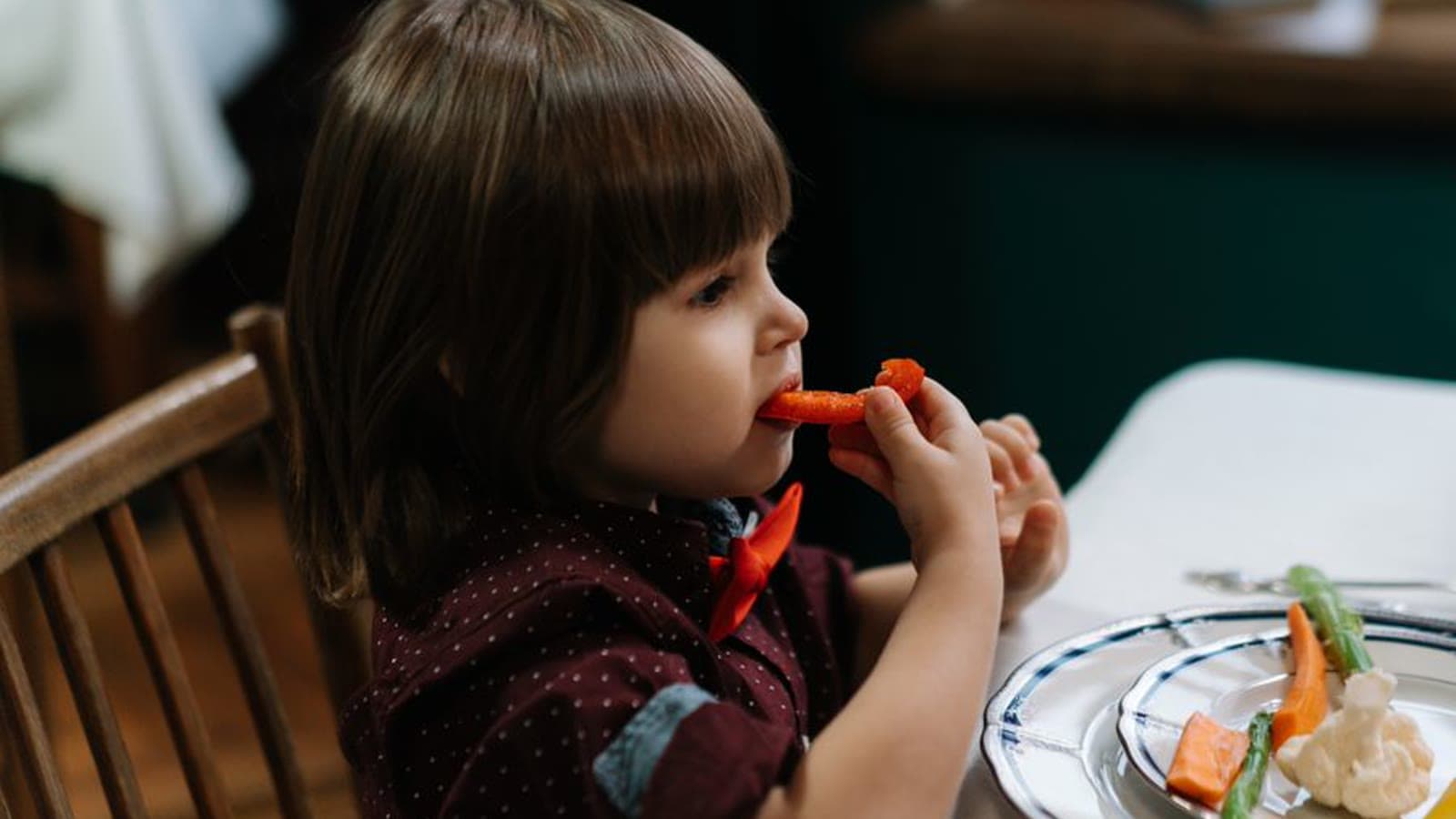 A toddler sitting at a dining table and eating vegetables