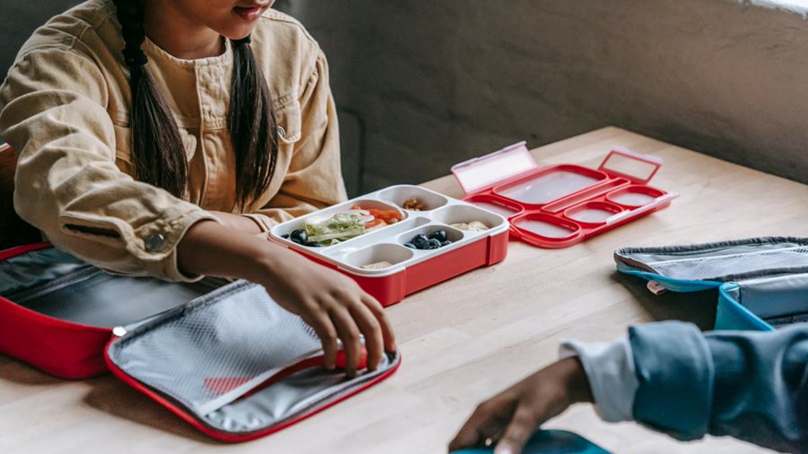Open colorful lunch boxes filled with snacks, held in children's hands