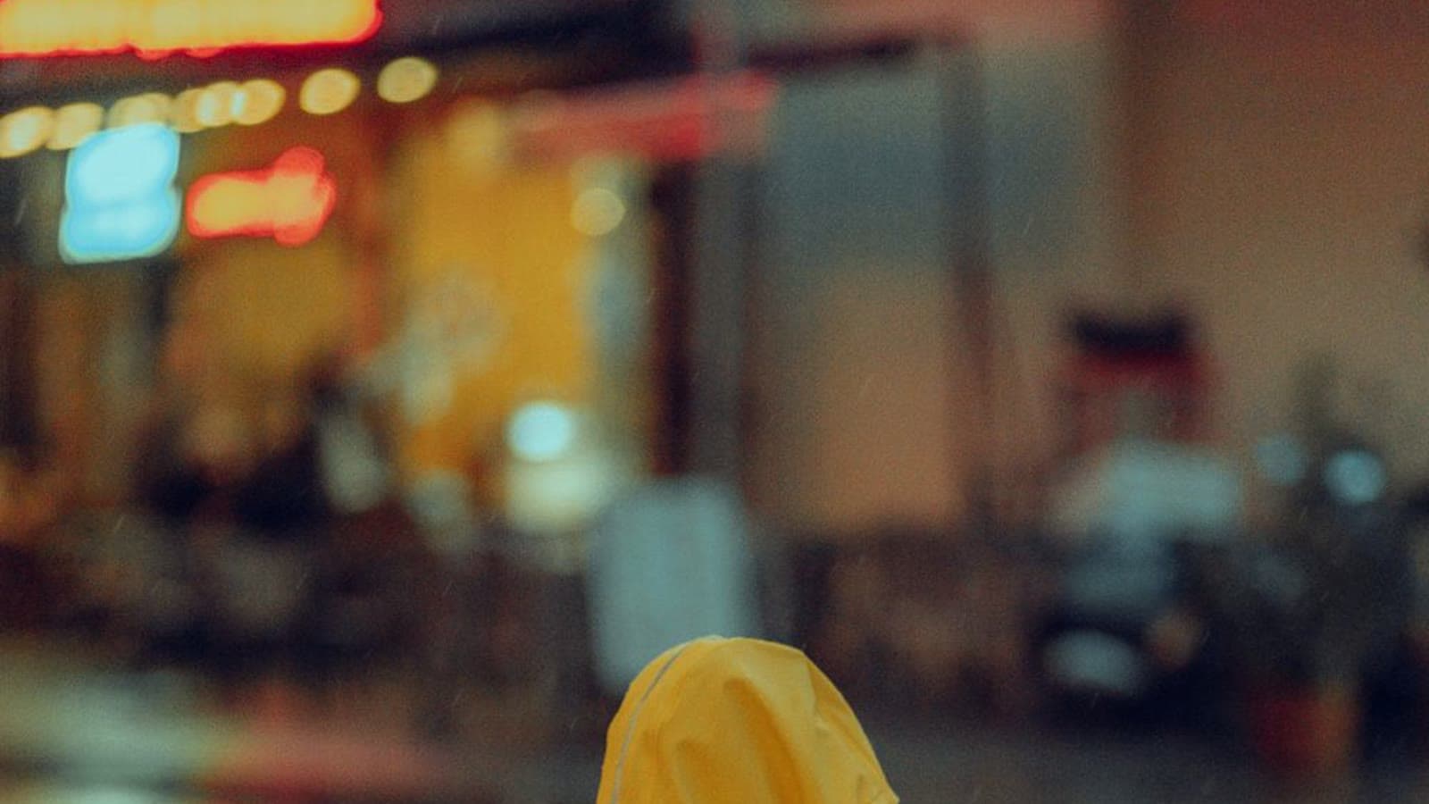 A child in a yellow raincoat and red rain boots standing in the rain