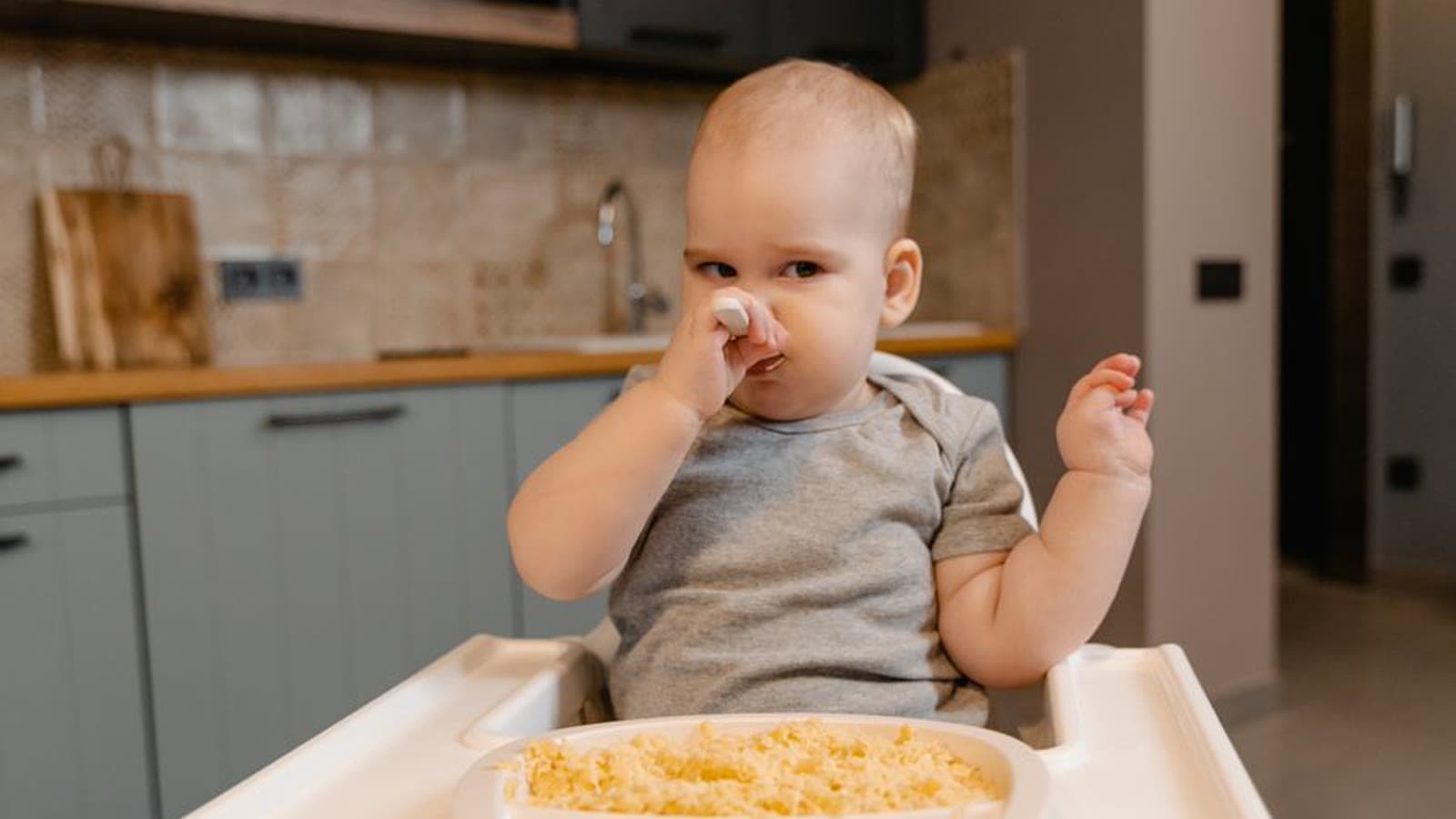 A baby in a high chair holding a spoon to their mouth