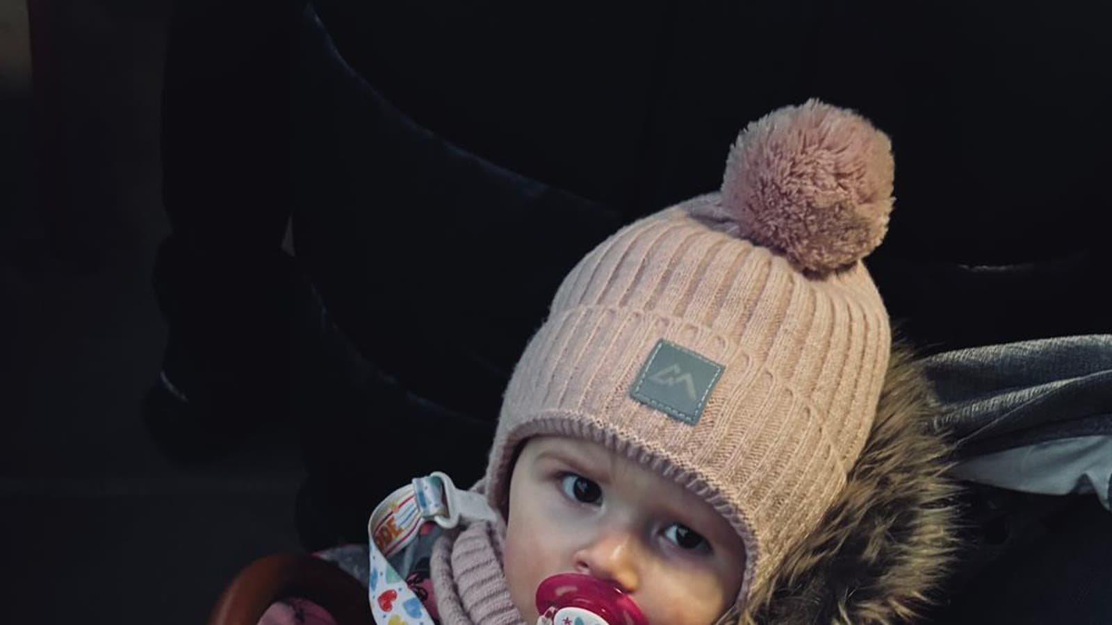 A baby bundled in a pink winter jacket and hat, sitting in a stroller