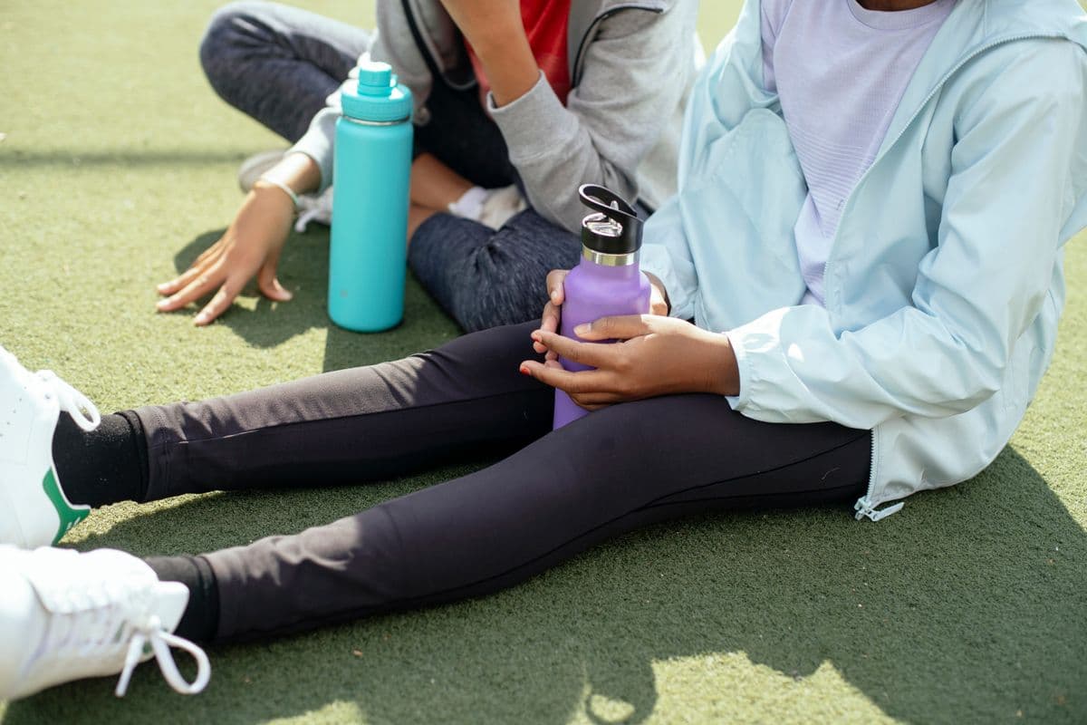 Two insulated kids' water bottles on the grass beside children