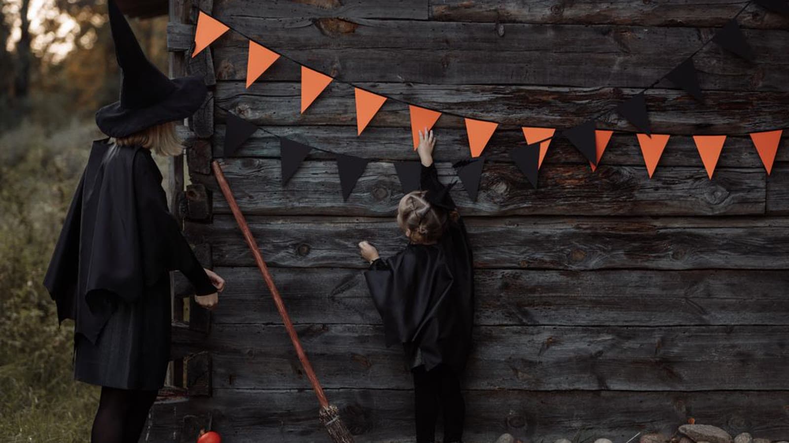 A mother and daughter in matching black witch costumes decorating for Halloween