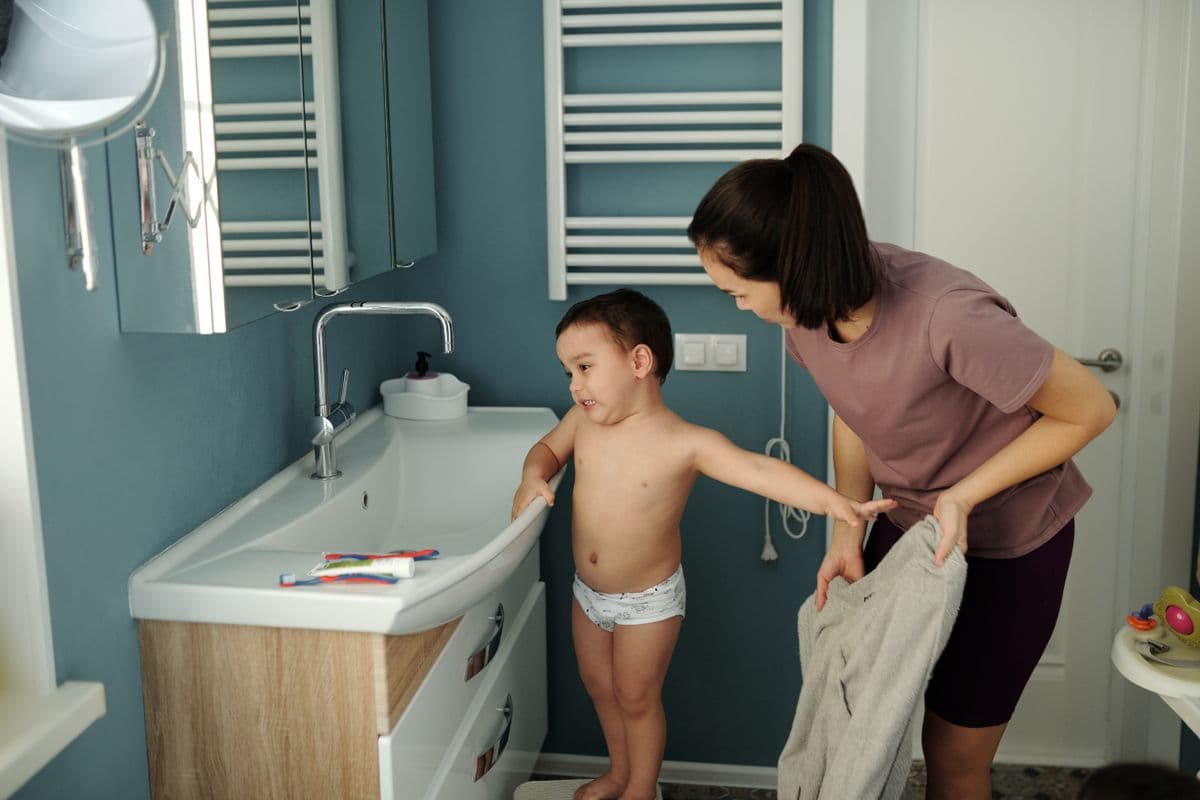 A mother helping her toddler, who is wearing training underwear, at the bathroom sink