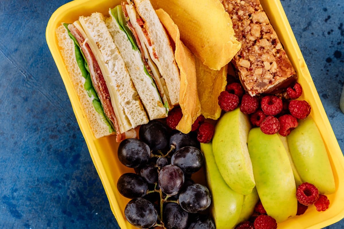 A packed lunch box with fruit, crackers, and a sandwich