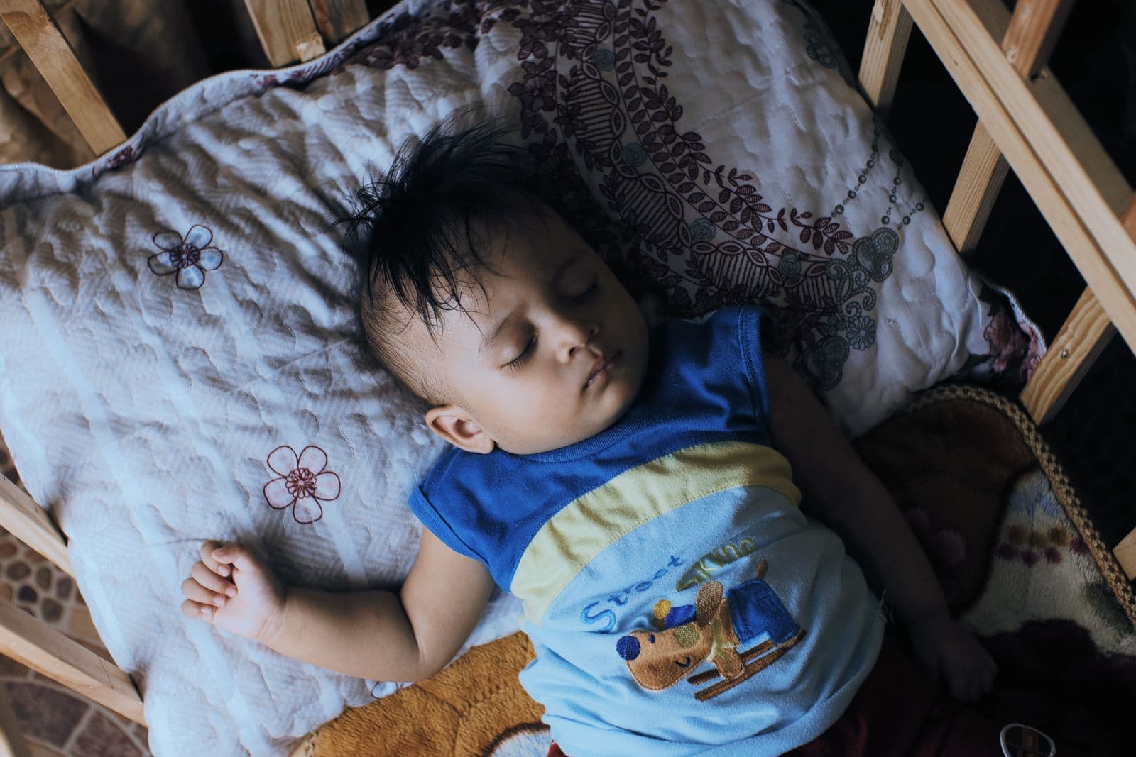 A toddler sleeping soundly in a wooden crib