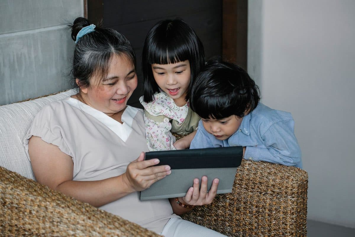 A grandmother sitting with grandchildren and sharing a tablet together at home