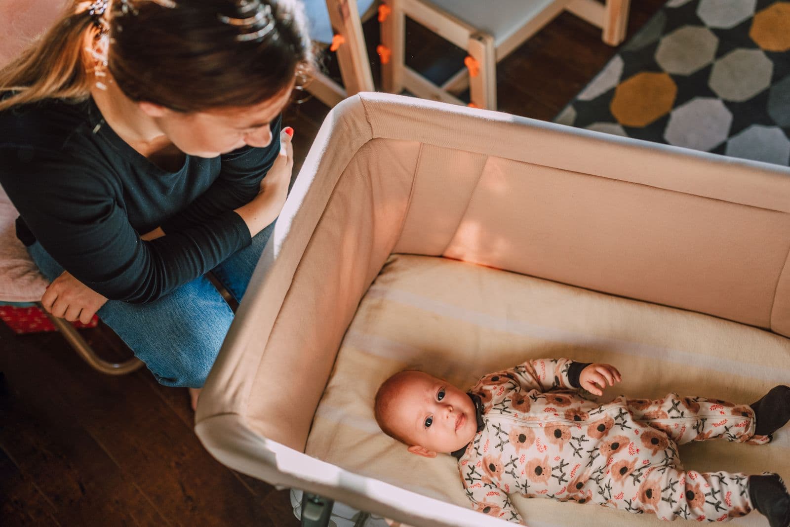 A parent looking down into a crib at a sleeping baby